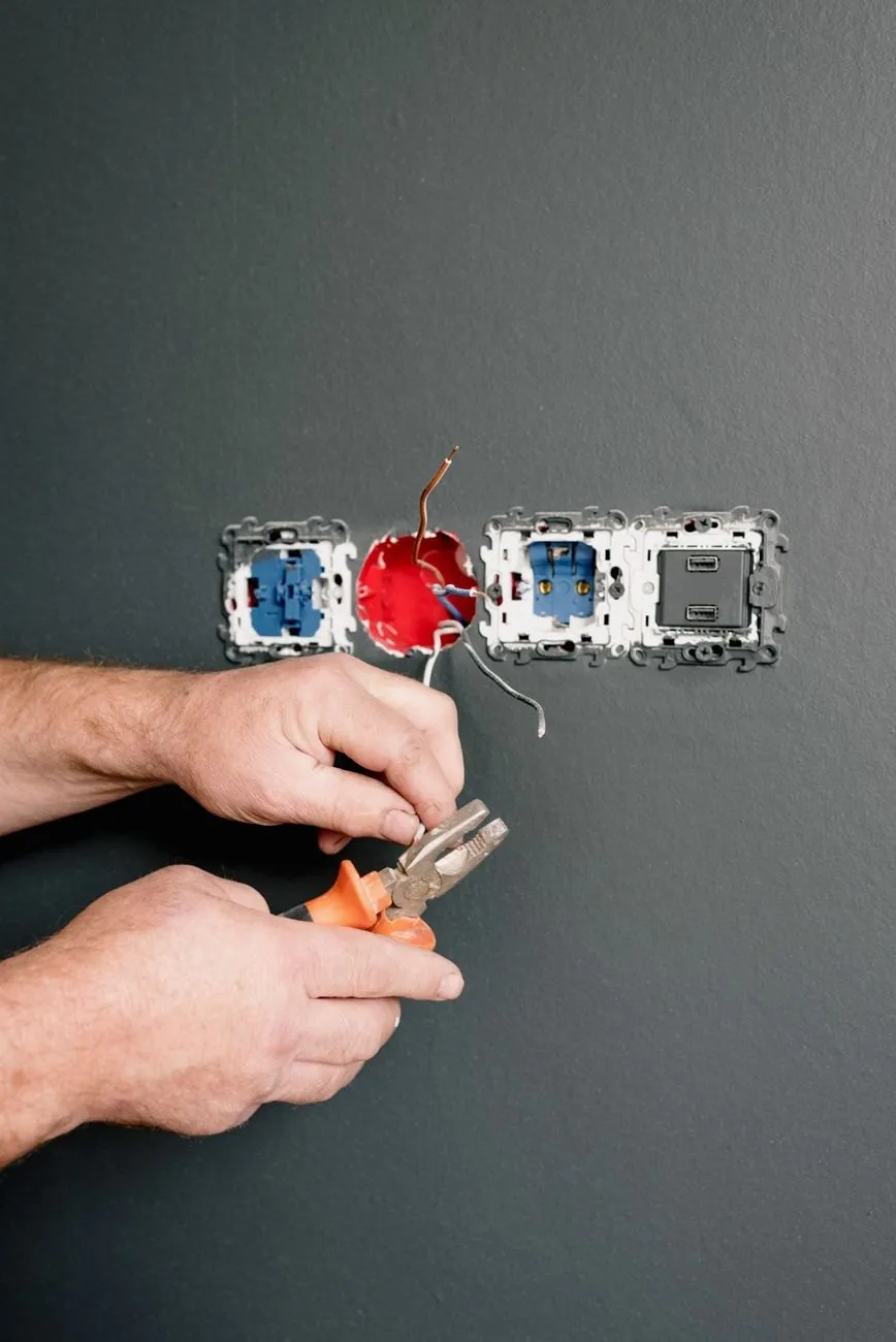 Hands using pliers to prepare a wire at a row of new sockets on a dark grey wall